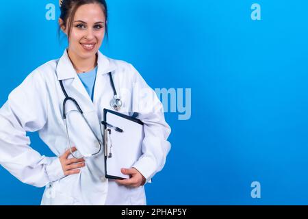 Eine Ärztin in einem medizinischen Kleid mit einem Klemmbrett und einem Stethoskop auf blauem Hintergrund Stockfoto