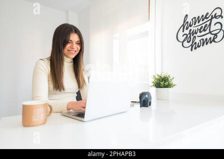 Eine junge Frau sitzt an einem Schreibtisch in einer gut beleuchteten Umgebung und arbeitet an ihrem Laptop Stockfoto
