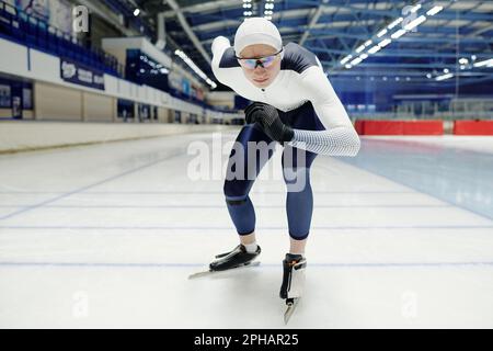 Junger Sportler in Uniform und Brille, der an der Startlinie auf Skates steht und sich während eines kurzen Speed Skating-Rennens vorwärts bewegt Stockfoto