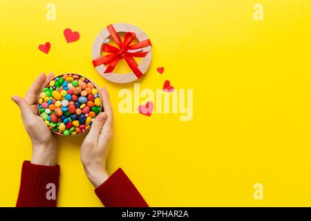 Weibliche Hände mit köstlichen Süßigkeiten in der Schachtel auf farbigem Hintergrund. Stockfoto
