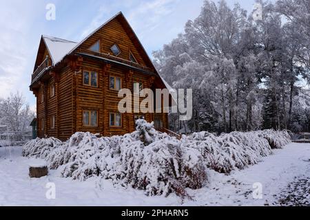 Eine große Holzhütte in einem Dorf in der Nähe von Büschen und Birken bedeckt mit weißem Schnee in Altai in Sibirien im Winter Stockfoto