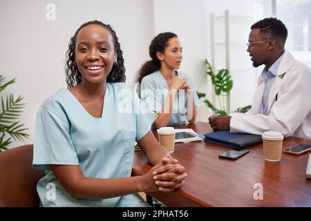 Porträt einer Krankenschwester oder eines Arztes in Peelings, die mit einem Kollegen am Sitzungstisch sitzen Stockfoto