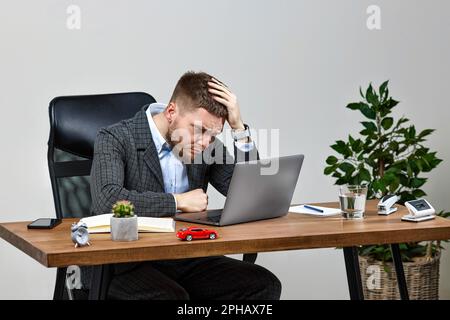 Mann sitzt auf einem Stuhl am Tisch und ruht sich aus, benutzt Laptop Stockfoto