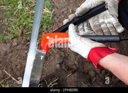 Nahaufnahme von Hand Verwenden Sie eine Nietpistole, um eine Gewächshaus-Metallkonstruktion zu montieren, und befestigen Sie sie mit Nieten. Stockfoto