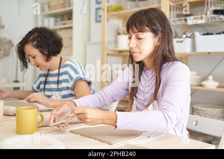 Frauen, die in einem Töpferkurs handgemachte Töpferwaren herstellen. Handwerk und Hobbys. Stockfoto