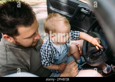 Papa zeigt seinem kleinen Sohn, wie er das Auto fährt, während er hinter dem Steuer sitzt Stockfoto