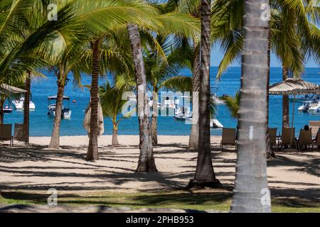 Blick auf einen Strand mit Palmen, Stühlen, Sonnenschirmen und Booten entlang der Pazifikküste Mexikos. Stockfoto