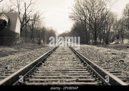 Ein malerisches, ländliches Dorf mit einer alten Eisenbahnstrecke, die durch das Zentrum verläuft, Graustufen Stockfoto