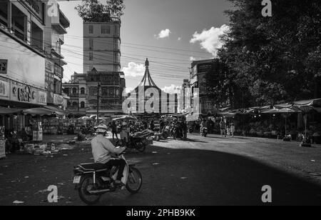 Ein Mann fährt mit dem Motorrad in Richtung der überfüllten Straßen vor dem Wahrzeichen Central Market in Pleiku im zentralen Hochland Vietnams. Stockfoto