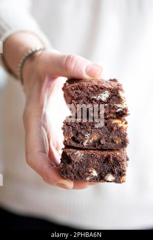 Eine Frau mit drei gestapelten, frisch gebackenen, dreifachen Schokoladenbrownies. Die Brownies sind frisch und lecker. Ein Genuss Stockfoto