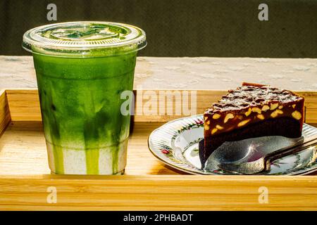 Bownie-Kuchen auf einem Blumenmuster-Teller, serviert mit grünem Tee Latte Stockfoto