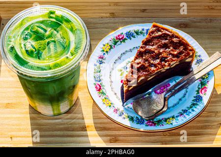 Bownie-Kuchen auf einem Blumenmuster-Teller, serviert mit grünem Tee Latte Stockfoto