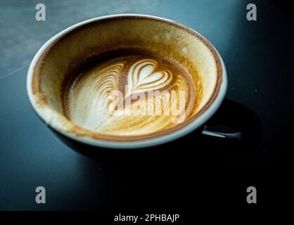 eine tasse heißen Latte-Kaffee mit herzförmiger Schaummilch auf dunklem Hintergrund Stockfoto