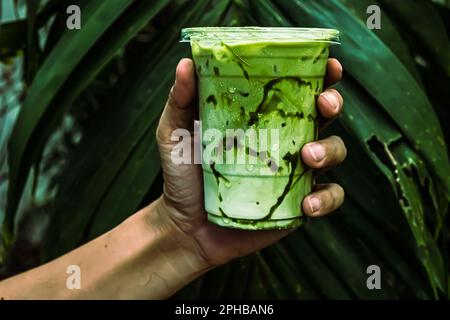 iced Green Matcha Tea gemischt mit Eiswürfel und Milch in Latte Glas mit grünem Naturhintergrund Stockfoto