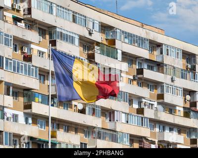 Rumänische Nationalflagge im Wind und ein abgenutztes kommunistisches Wohnhaus im Hintergrund, in Bukarest Rumänien. Stockfoto