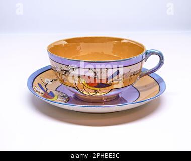 Antike Teetasse und Untertasse vor weißem Hintergrund. Hergestellt in Japan. Mit einem roten, gelben und blauen Vogel. Stockfoto