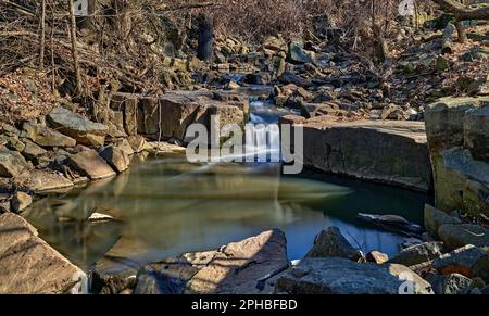 Eine lange Exposition von Wolf Creek ein fließender Bach mit kleinen Wasserfällen, die sich in einen gläsernen Wasserpool leeren. In Ridgefield, New Jersey, USA. Stockfoto
