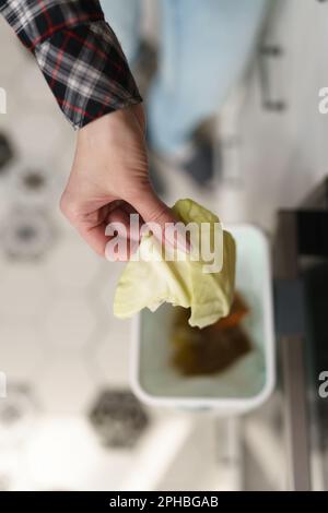 Eine Frau, die organische Lebensmittelabfälle in einen bokashi-Behälter wirft. Frau, die Kohlblätter für Kompost in den Abfalleimer wirft. Person, die biologisch abbaubare Stoffe kompostiert t Stockfoto