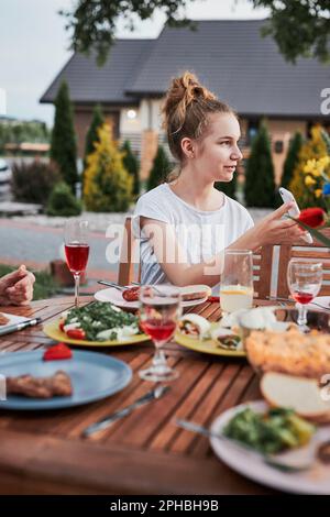 Familie mit einer Mahlzeit vom Grill während des Sommer Picknick im Freien Abendessen in einem Hausgarten. Nahaufnahme von Leuten, die an einem Tisch mit Essen und Geschirr sitzen Stockfoto