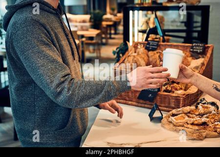 Ein Mann, der Kaffee und Gebäck zum Mitnehmen im Café kauft. Mann steht an der Theke und nimmt eine Kaffeetasse vom Barista Stockfoto