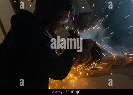 Ein Mann, der mit einem Winkelschleifer arbeitet, wird von Funken umschlossen, die von der Trennscheibe herabfliegen Stockfoto