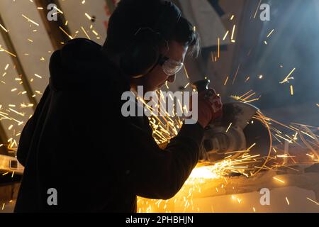 Ein Mann, der mit einem Winkelschleifer arbeitet, wird von Funken umschlossen, die von der Trennscheibe herabfliegen Stockfoto