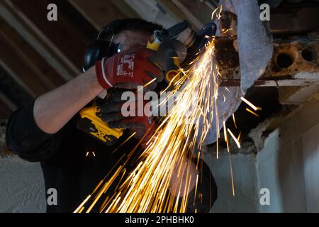 Ein Mann, der mit einem Winkelschleifer arbeitet, wird von Funken umschlossen, die von der Trennscheibe herabfliegen Stockfoto