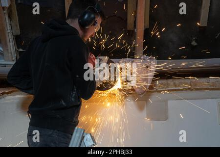 Ein Mann, der mit einem Winkelschleifer arbeitet, wird von Funken umschlossen, die von der Trennscheibe herabfliegen Stockfoto