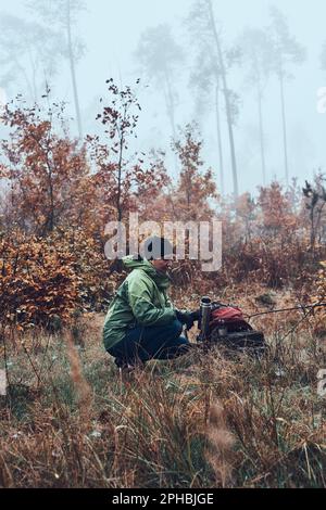 Frau mit Rucksack, die während der Herbstreise eine Pause hat und am kalten Herbsttag ein heißes Getränk aus einer Thermoskanne trinkt. Eine aktive Frau mittleren Alters, die um sich herumwandert Stockfoto