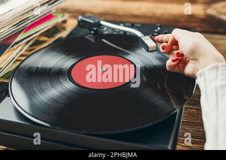 Junge Frau, die Musik von einem Plattenspieler hört. Wiedergabe von Musik auf Plattenspielern. Frau, die zu Hause Musik aus der alten Plattensammlung genießt. Stockfoto