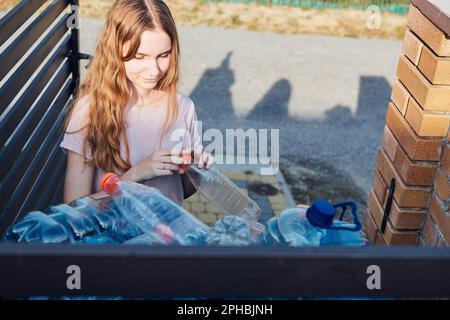 Junge Frau wirft leere gebrauchte Plastikwasserflaschen in den Abfalleimer. Sammeln von Kunststoffabfällen zum Recycling. Konzept der Plastikverschmutzung und auch Stockfoto