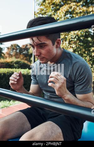 Junger Mann macht Sit-ups während seines Trainings in einem modernen Calisthenics Street Workout Park. Mann, der auf einem Sit-up-Board sitzt und Sportkleidung trägt Stockfoto