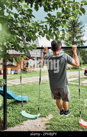 Junger Mann, der während seines Calisthenics-Trainings auf einem Camping während seiner Sommerurlaubsreise an der hochgeklappten horizontalen Stange zieht Stockfoto