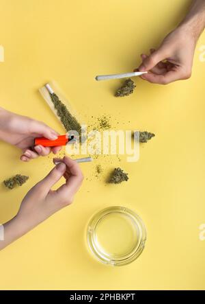 Trockene Knospen von medizinischem Marihuana, zerdrücktes Marihuana auf dem Papier. In Frauenhänden gibt es ein Gelenk und ein Feuerzeug, ein Gelenk in der Hand eines Mannes. Neben einem Glas Stockfoto