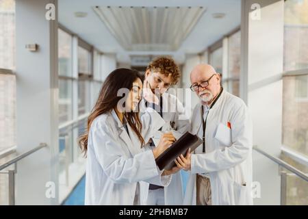 Ärztin diskutiert über ein digitales Tablet mit männlichen Kollegen im Korridor des Krankenhauses Stockfoto