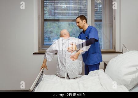 Männliche Krankenschwester hilft Seniorpatienten im Krankenhaus auf dem Bett zu sitzen Stockfoto