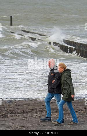 Ältere Ehepaare, die an einem windigen Tag während des Wintersturms in Zeeland, Niederlande, entlang der Nordseeküste spazieren Stockfoto