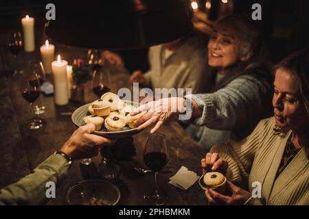 Seniorin nimmt Törtchen vom Teller während der Dinnerparty Stockfoto