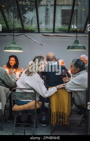 Seniorin sitzt auf einem Stuhl, während sie mit einer pensionierten Freundin auf der Dinnerparty spricht Stockfoto
