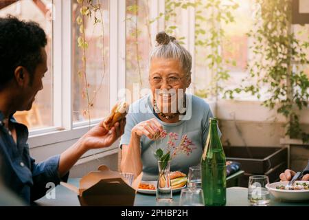 Glückliche Seniorin, die zusammen mit einem männlichen Freund im Restaurant isst Stockfoto