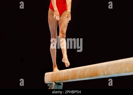 Beine weibliche Turnerin in rotem Badeanzug trainieren Balance Strahlgymnastik auf dunklem Hintergrund, olympische Sportarten sind in Sommerspielen enthalten Stockfoto