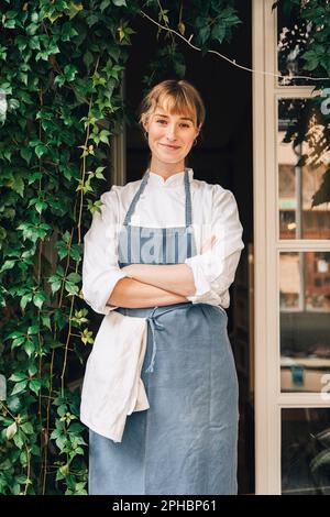 Porträt einer lächelnden Chefköchin, die vor dem Restaurant mit gekreuzten Armen steht Stockfoto