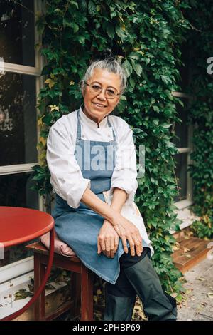 Portrait einer lächelnden Chefköchin, die vor dem Restaurant sitzt Stockfoto