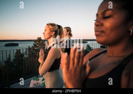 Eine Frau mit gefalteten Händen, die mit Freundinnen auf der Terrasse trainiert Stockfoto