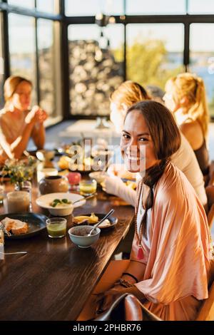 Portrait einer glücklichen Frau, die mit Frühstück auf dem Esstisch im Retreat Center sitzt Stockfoto