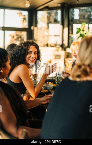 Porträt einer lächelnden jungen Frau, die mit ihren Freundinnen sitzt, während sie im Rückzugszentrum frühstückt Stockfoto