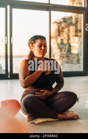 Übergroße Frau meditiert, während sie im Rückzugszentrum mit gekreuzten Beinen sitzt Stockfoto