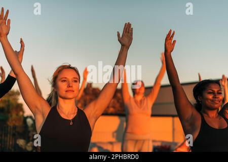 Eine Frau mit erhobenen Armen, die bei Sonnenuntergang mit einer Freundin trainiert Stockfoto