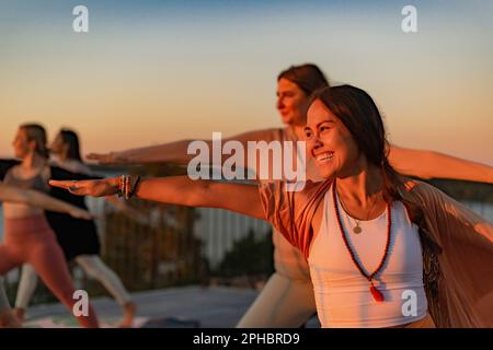 Glückliche Frau, die bei Sonnenuntergang Yoga mit einer Freundin auf der Terrasse macht Stockfoto