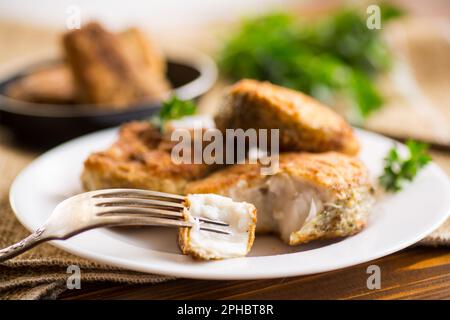 Ein Stück Seehecht, gebraten in knuspriger Kruste, auf einem Teller auf einem Holztisch. Stockfoto